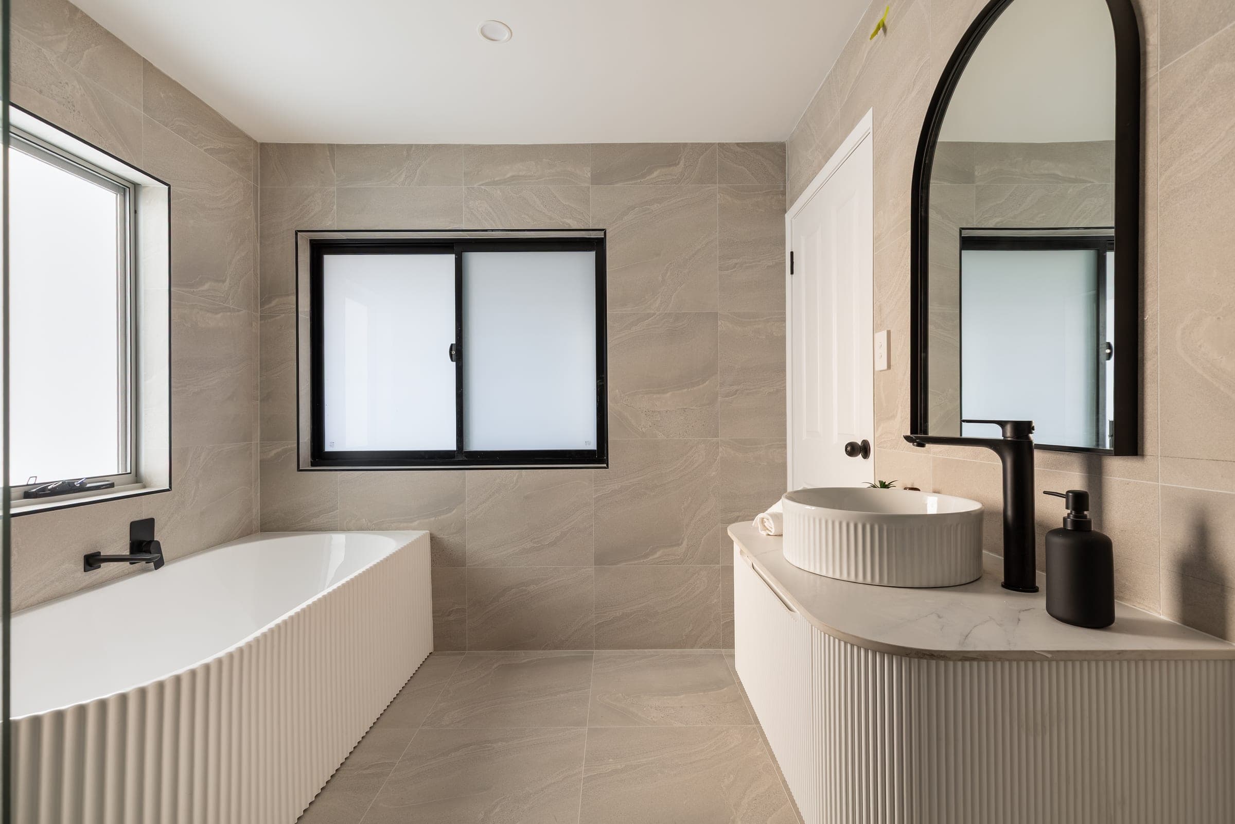 A bathroom with a freestanding bath, fluted vanity and arched mirror