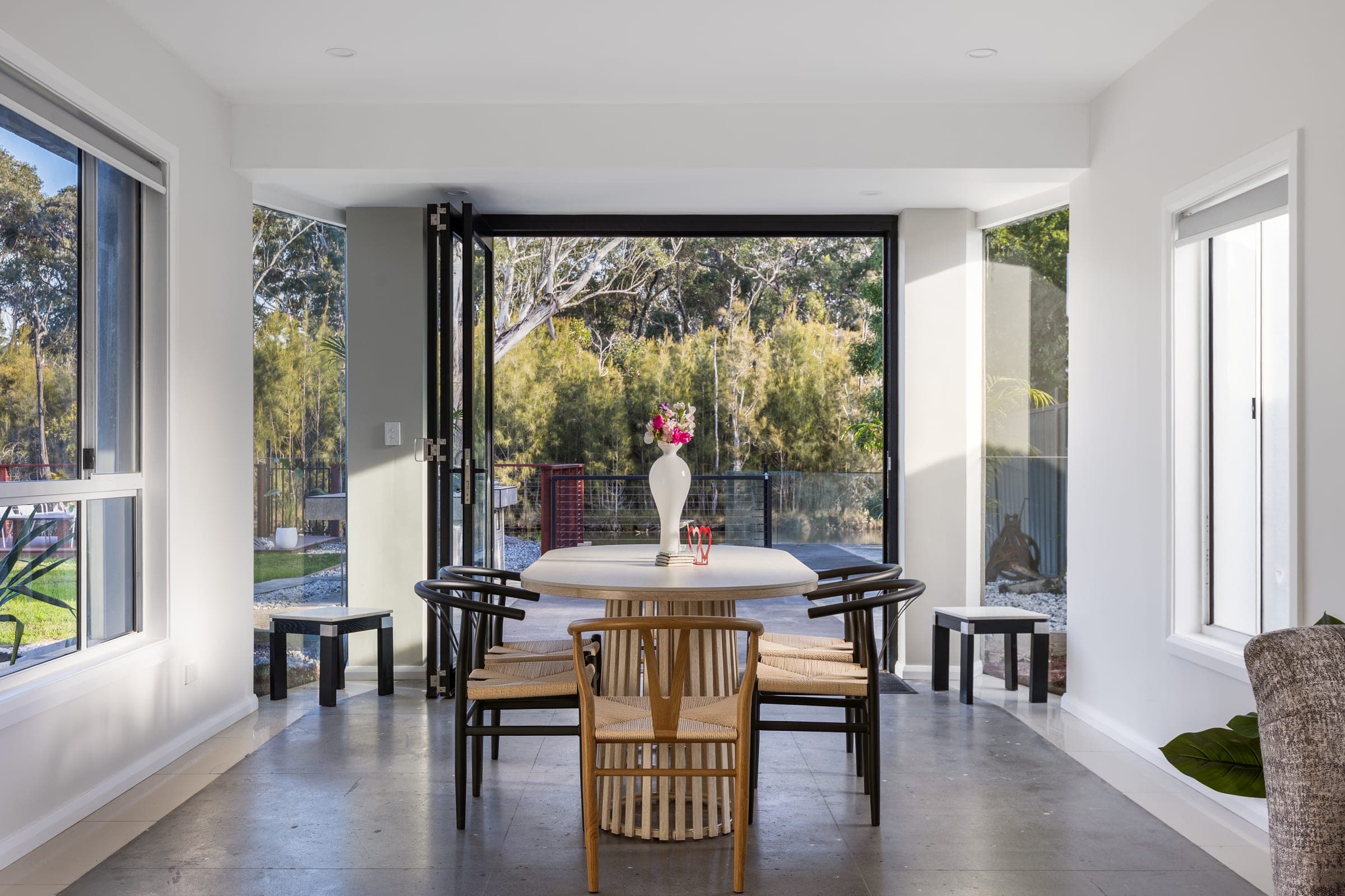 A dining table set in front of bifold doors opening onto bushland